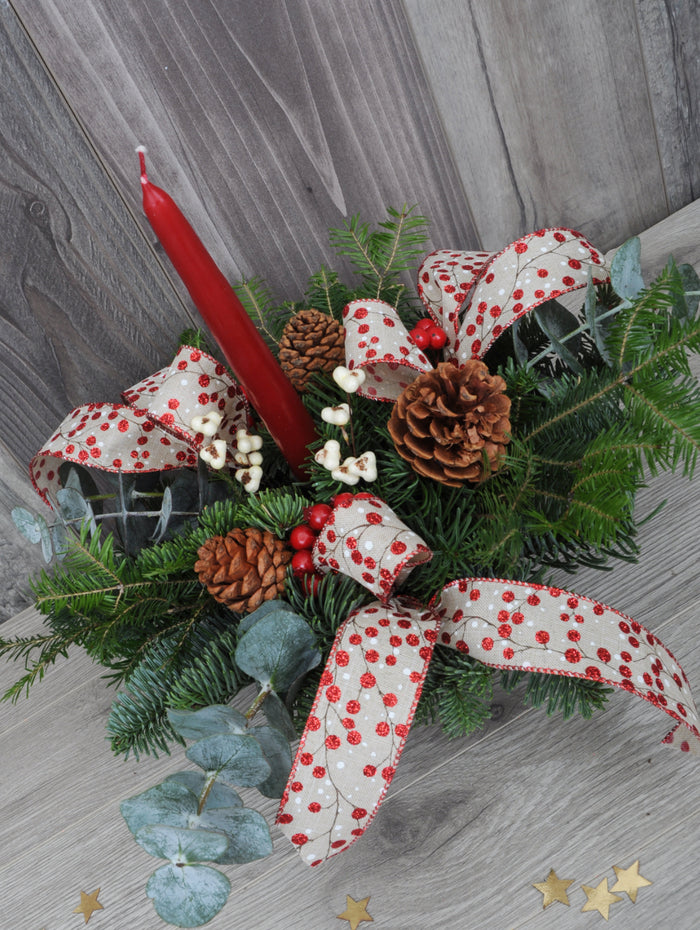 Centre de table de Noël avec une bougie rouge, des rubans et des baies.