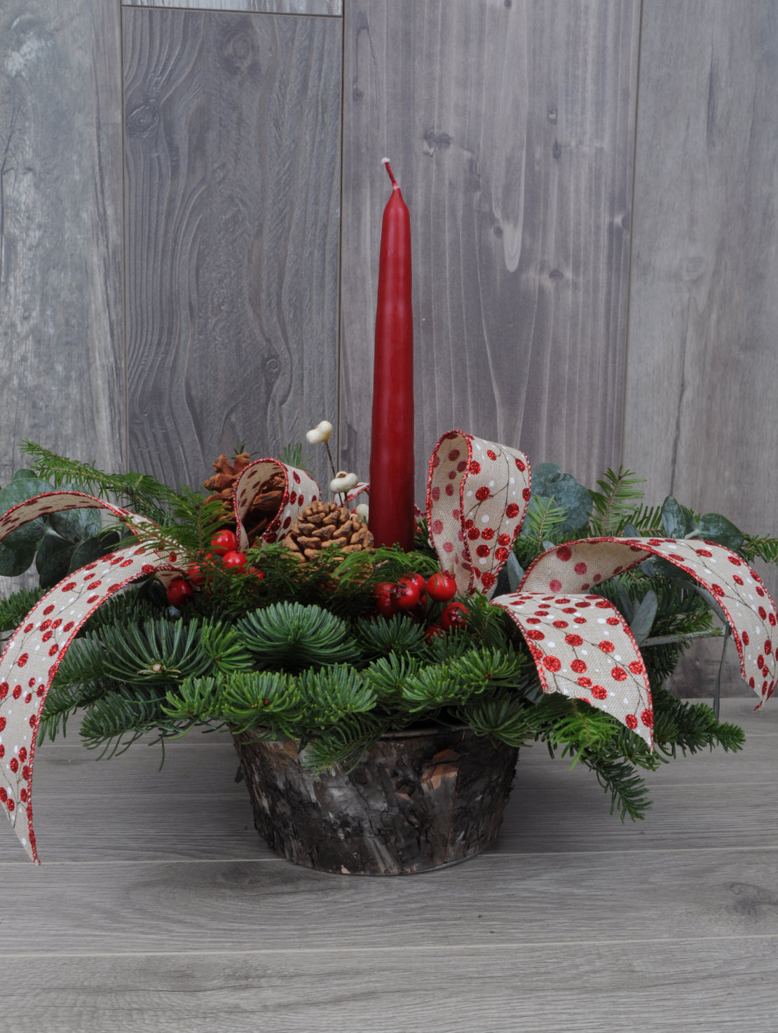 centre de table de Noël avec une bougie rouge, des rubans et des baies.
