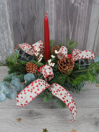 centre de table de Noël avec une bougie rouge, des rubans et des baies.