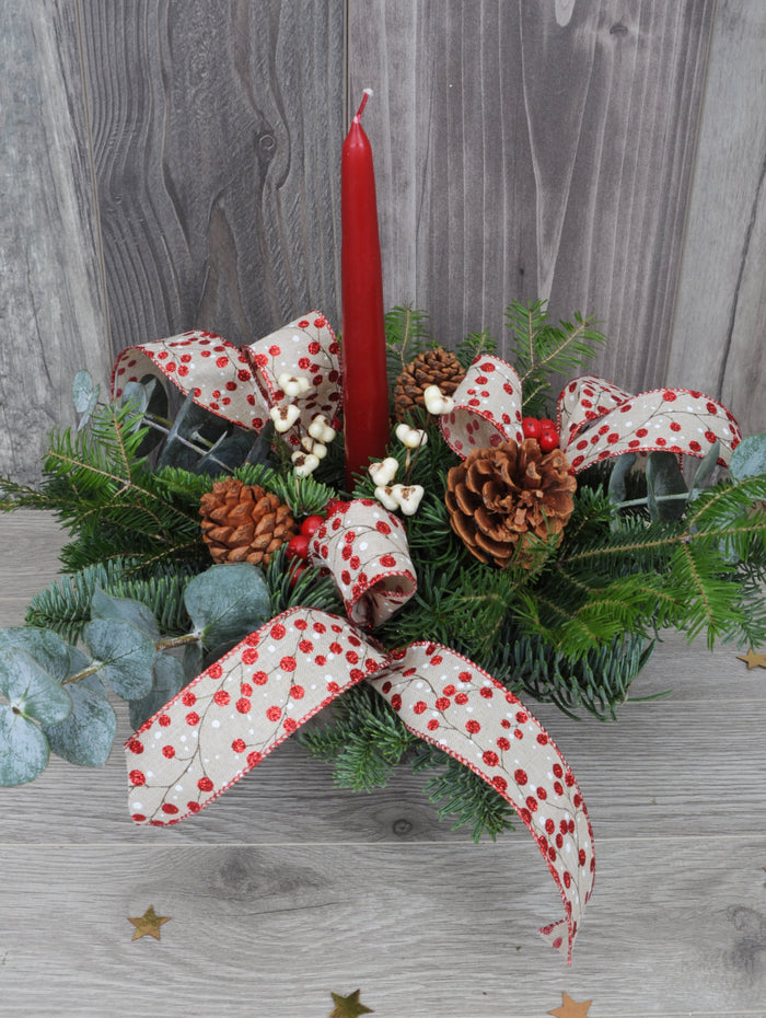 centre de table de Noël avec une bougie rouge, des rubans et des baies.